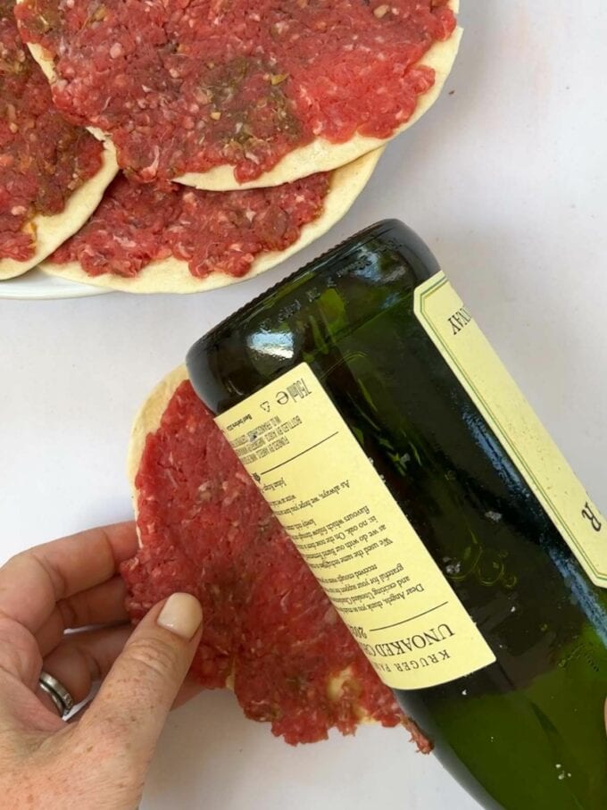 Rolling beef patties onto a tortilla wrap with a wine bottle to flatten it for the recipe Big Mac Tacos.