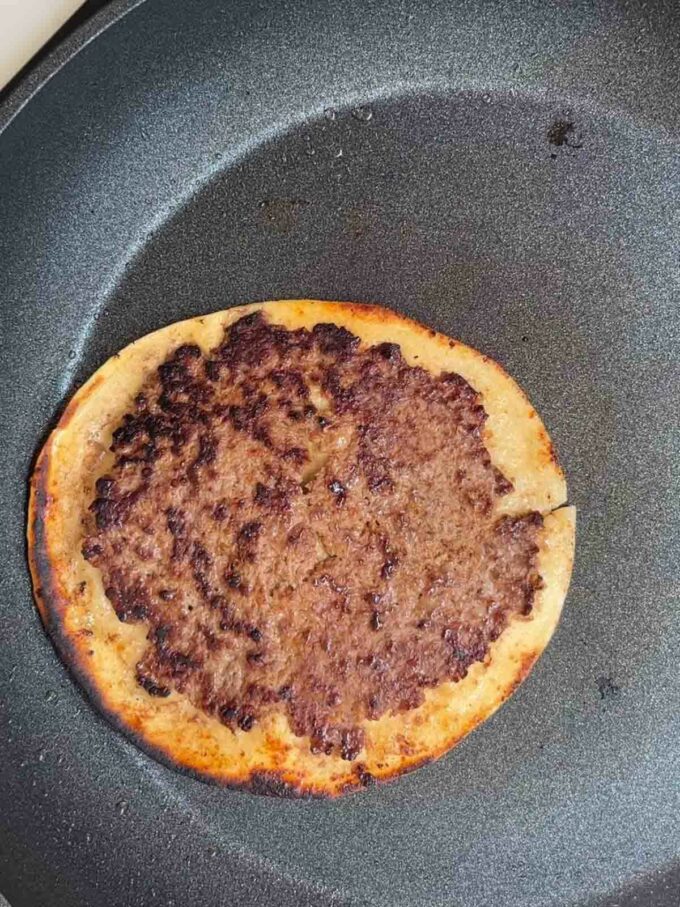 Beef patties on tortilla wrap being fried in a pan for the recipe Big Mac Tacos.