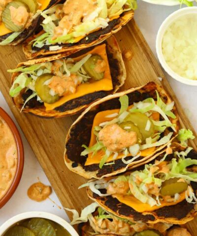 Big mac tacos on a serving board filled with cheese, lettuce, gherkins, onion and dressing.