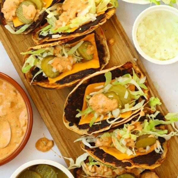 Big mac tacos on a serving board filled with cheese, lettuce, gherkins, onion and dressing.