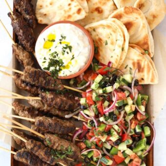 Lamb kofta kebabs recipe with flatbreads and Greek salad and tzatziki on a serving board, ready to eat.