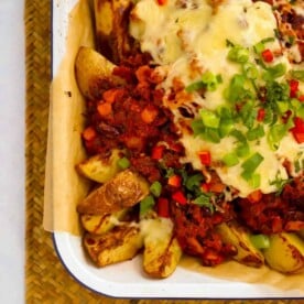 An oven tray filled with cooked homemade potato wedges and chilli con carne over the top with cheese and spring onion. Ready to serve.