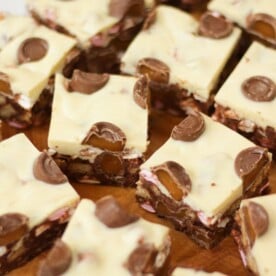 Side angle photo of Rolo Rocky Road Squares made with Roll Rocky Road Recipe, topped with white chocolate and Rolls on a wooden board.