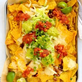 A tray filled with veggie loaded nachos, topped with salsa and guacamole.