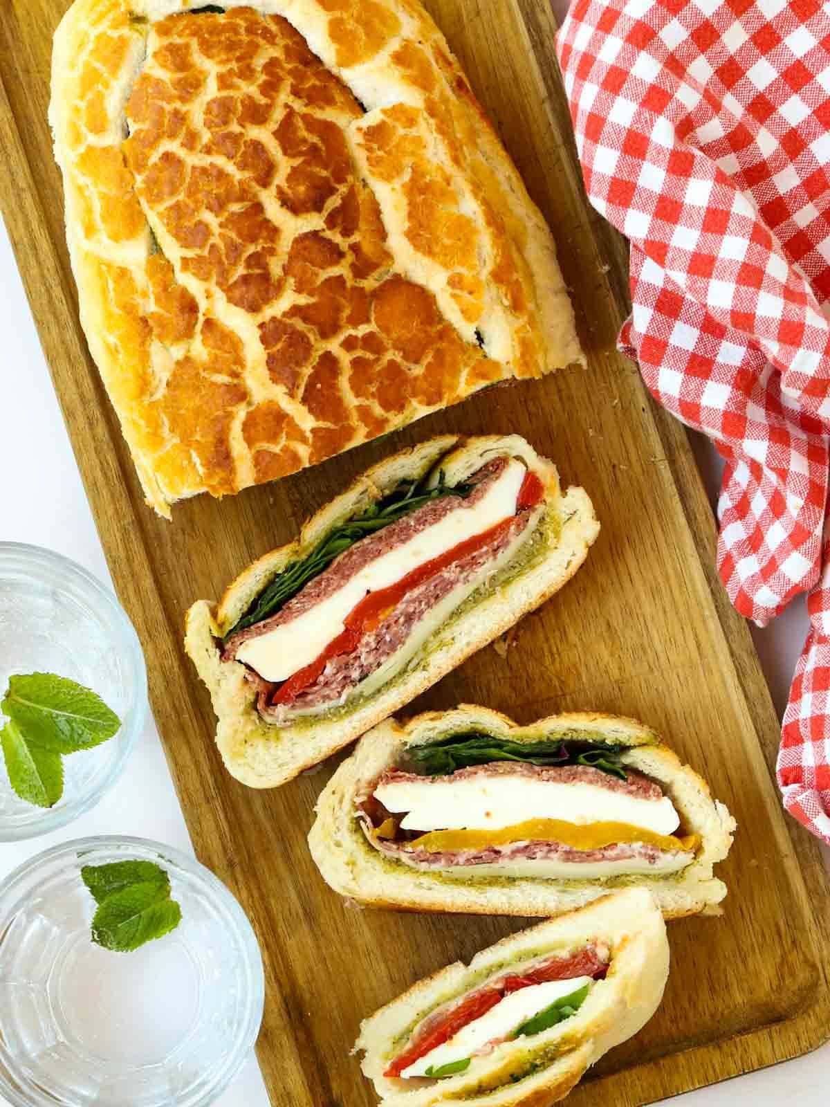 A stuffed picnic loaf, half sliced, laid on a board and ready to serve.