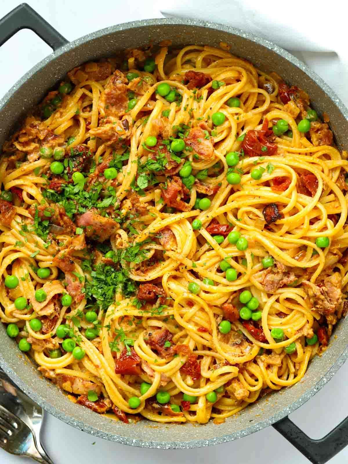 A big pan filled with spaghetti and bacon with peas for the recipe Creamy Bacon Pasta.