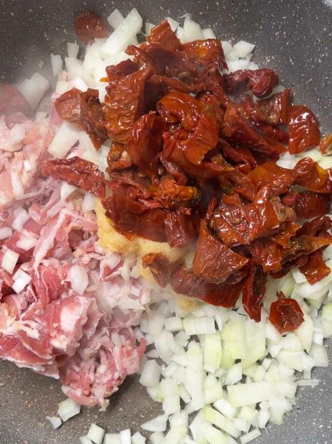 Sun-dried tomatoes in a pan with onion and bacon for the recipe Bacon Pasta. Step 2.