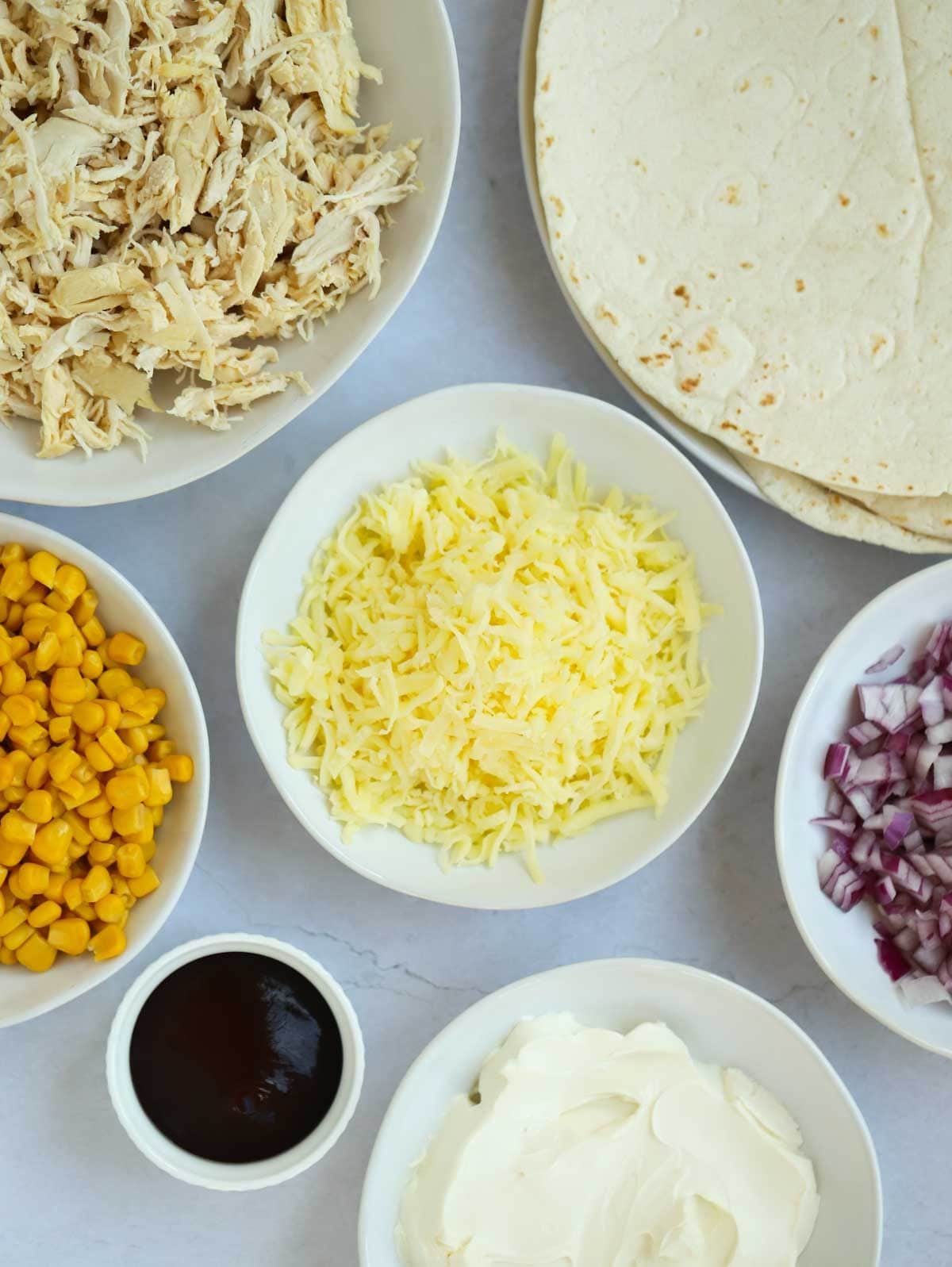 The ingredients for chicken wraps laid out in bowls on a counter top.