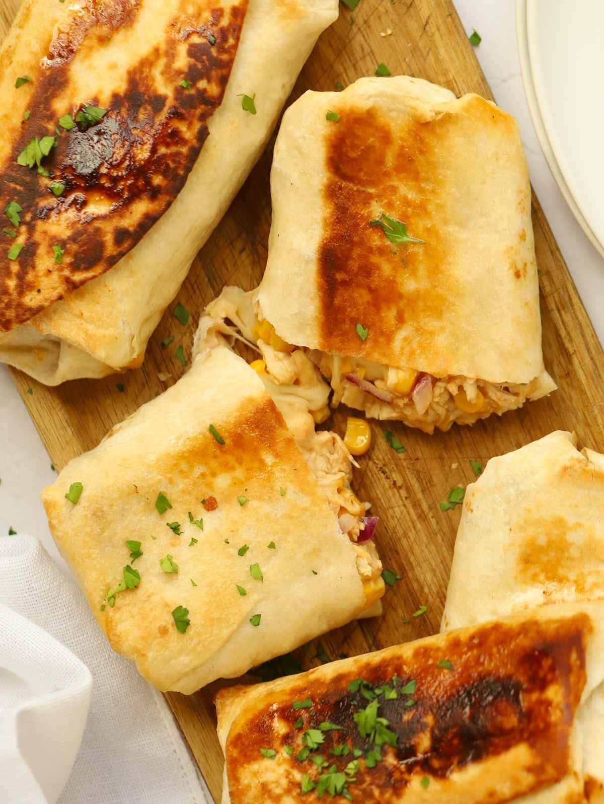 Fried chicken wraps cut in half and laid on a wooden chopping board.