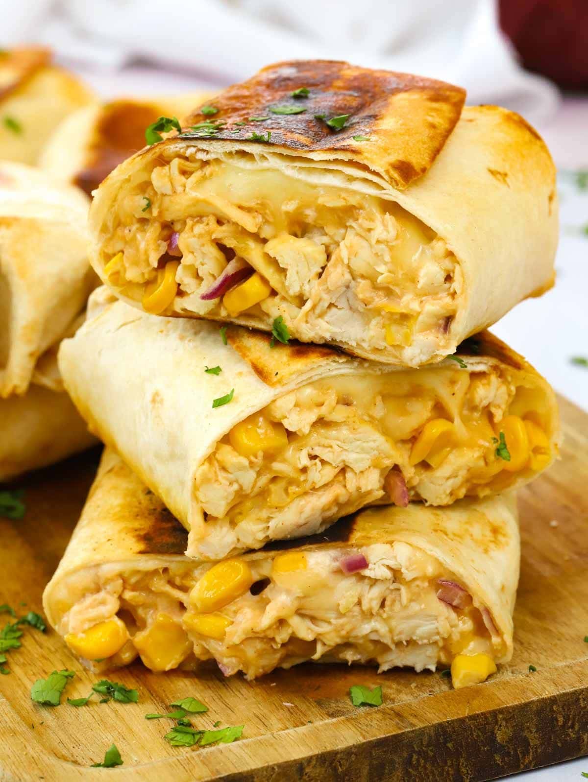 A side view of sliced chicken wraps with cooked chicken, cheese and sweetcorn inside, stacked up.