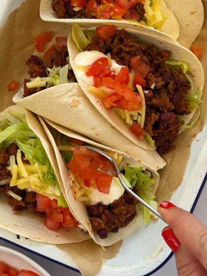 Beef Tacos being topped with tomato and salad, ready to serve.