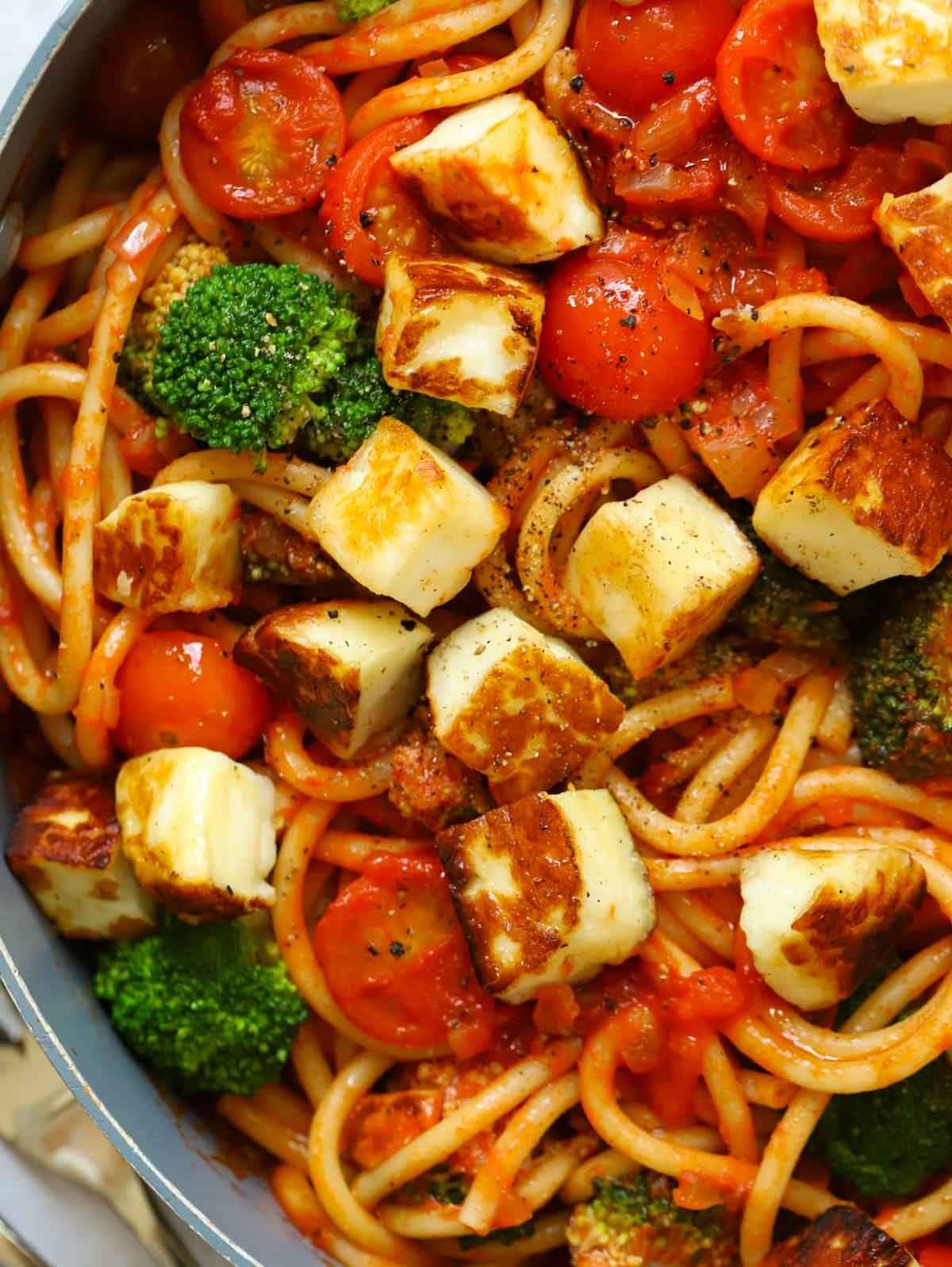 A close up of halloumi chunks with spaghetti and broccoli in a tomato sauce.