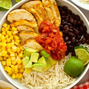 A big bowl filled with chicken, beans, rice, salsa, guacamole, lime and sweetcorn for the recipe No Cook Burrito Bowls.