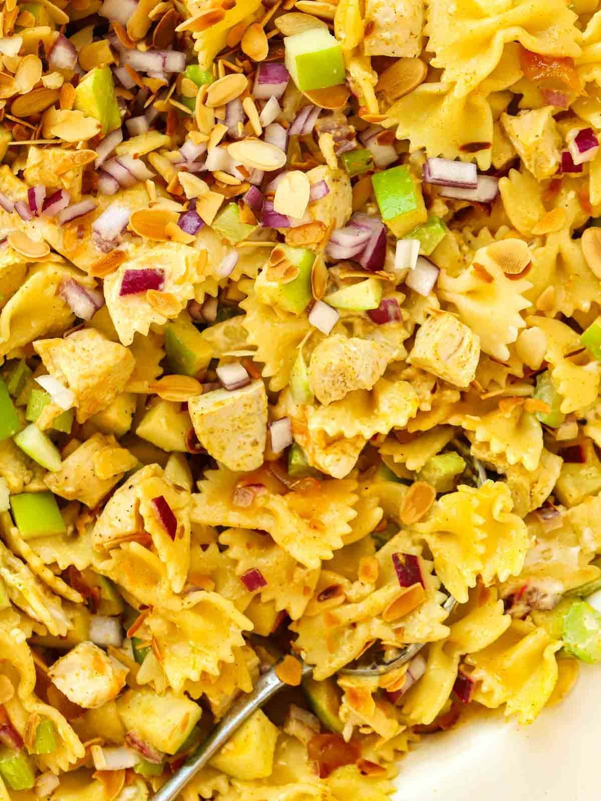 A close up of a Chicken Pasta Salad in a bowl, with a mixture of chicken, pasta, onion, apple and celery with a Coronation Chicken-style dressing.