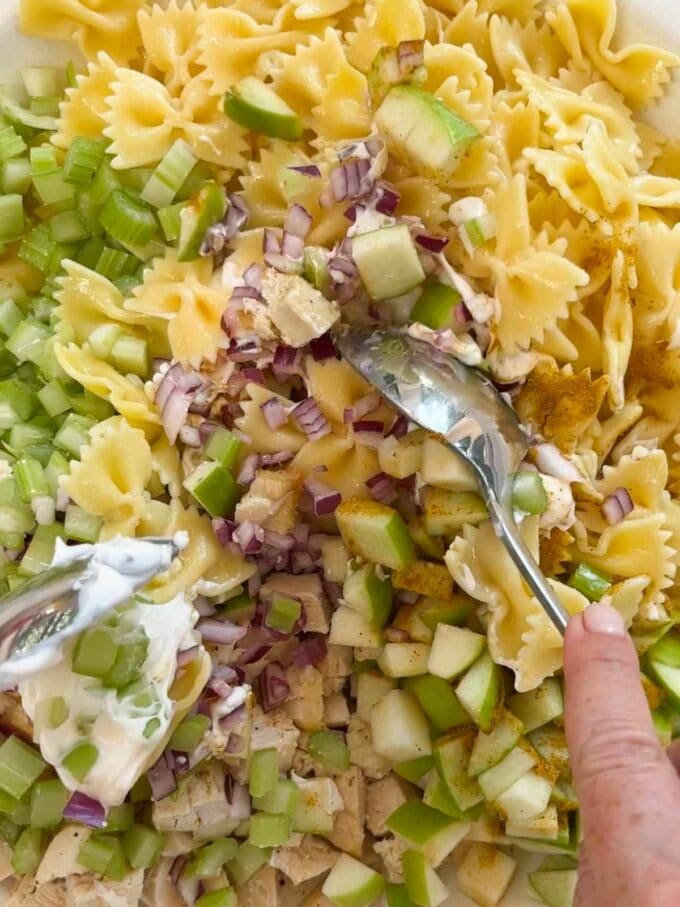Two spoons mixing together the ingredients for a chicken pasta salad.