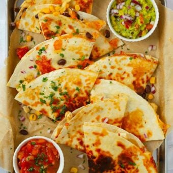 Quartered chicken quesadillas on a baking tray with dips.
