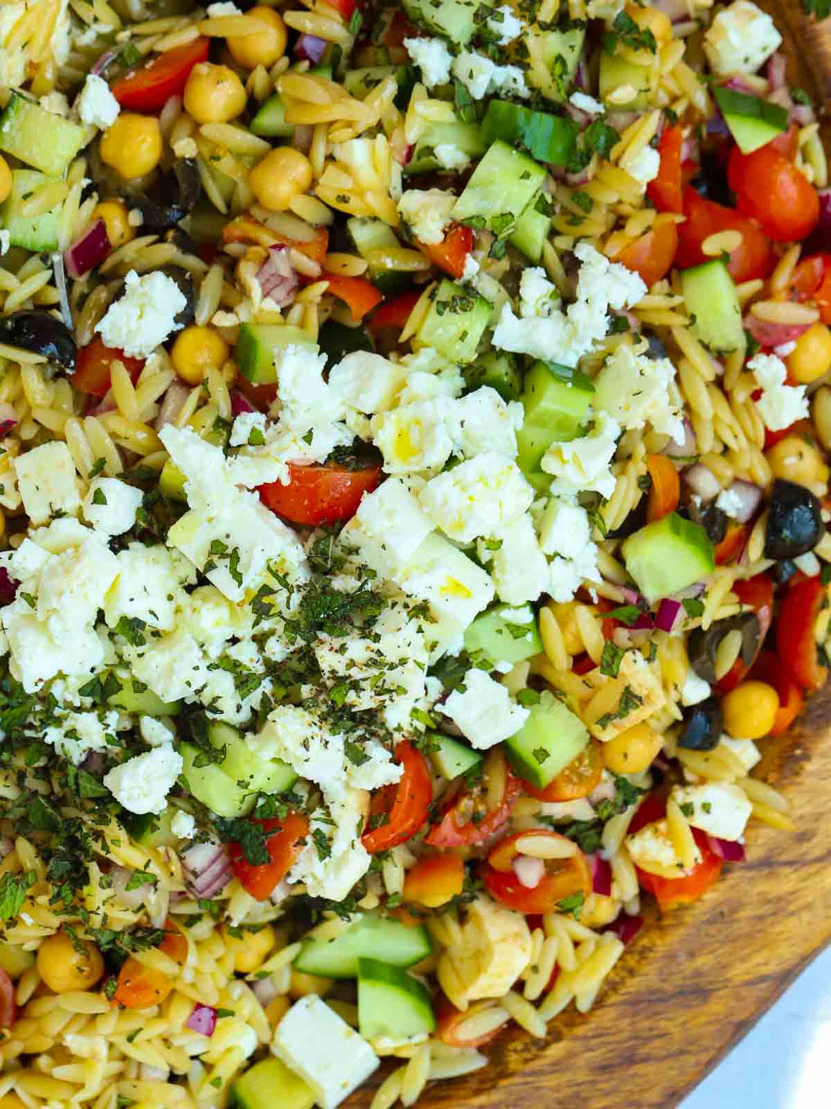 A big bowl filled with finely sliced ingredients that make up an Orzo Pasta Salad.