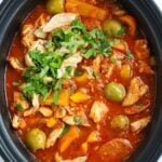 A big slow cooker pot filled with cooked Spanish-style chicken and chorizo stew, with olives and peppers.