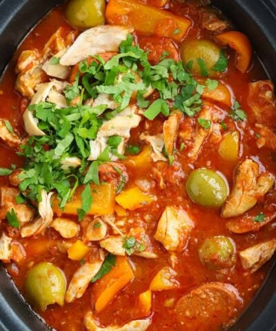 A big slow cooker pot filled with cooked Spanish-style chicken and chorizo stew, with olives and peppers.