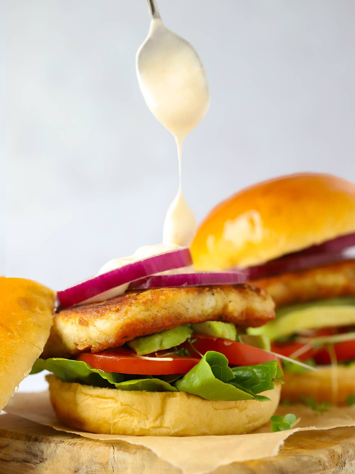 A spoon dripping sweet chilli mayo onto a halloumi burger with red onions on on a bun.