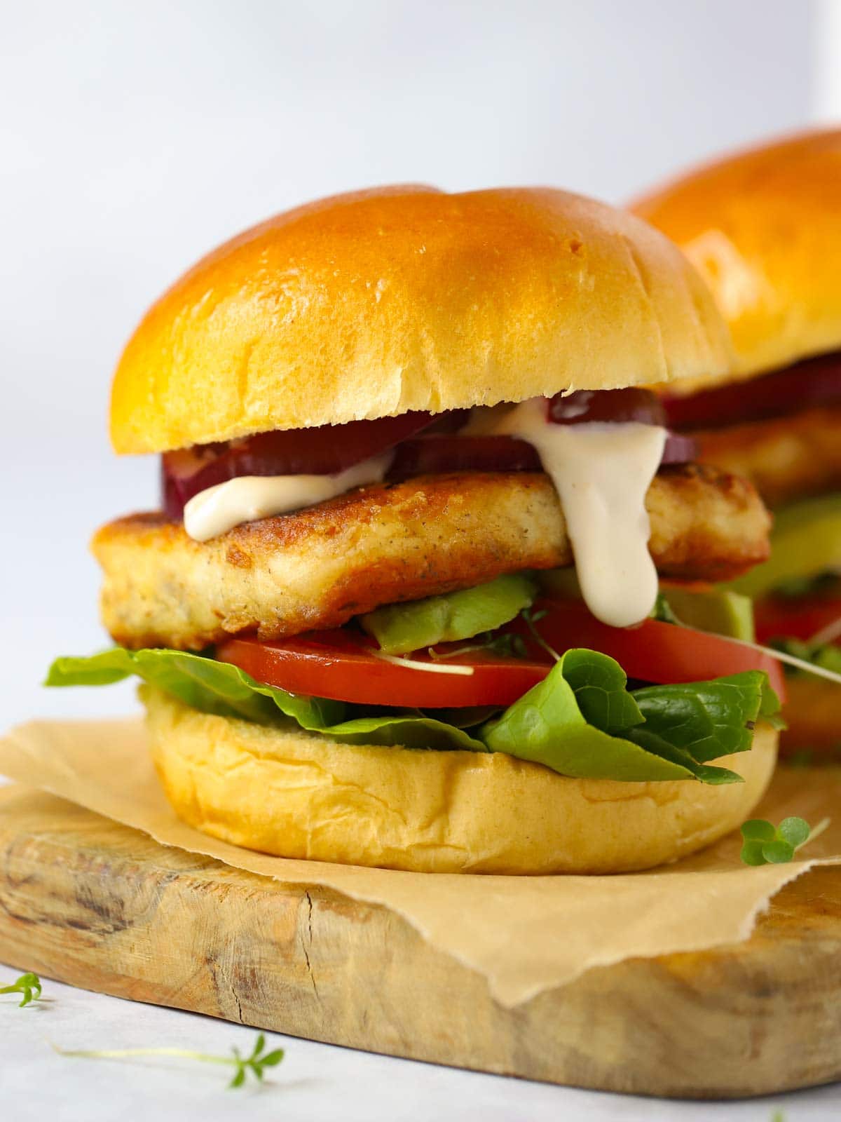 Really easy to make halloumi burger recipe, shown in a bun with sauce dripping on a wooden board.
