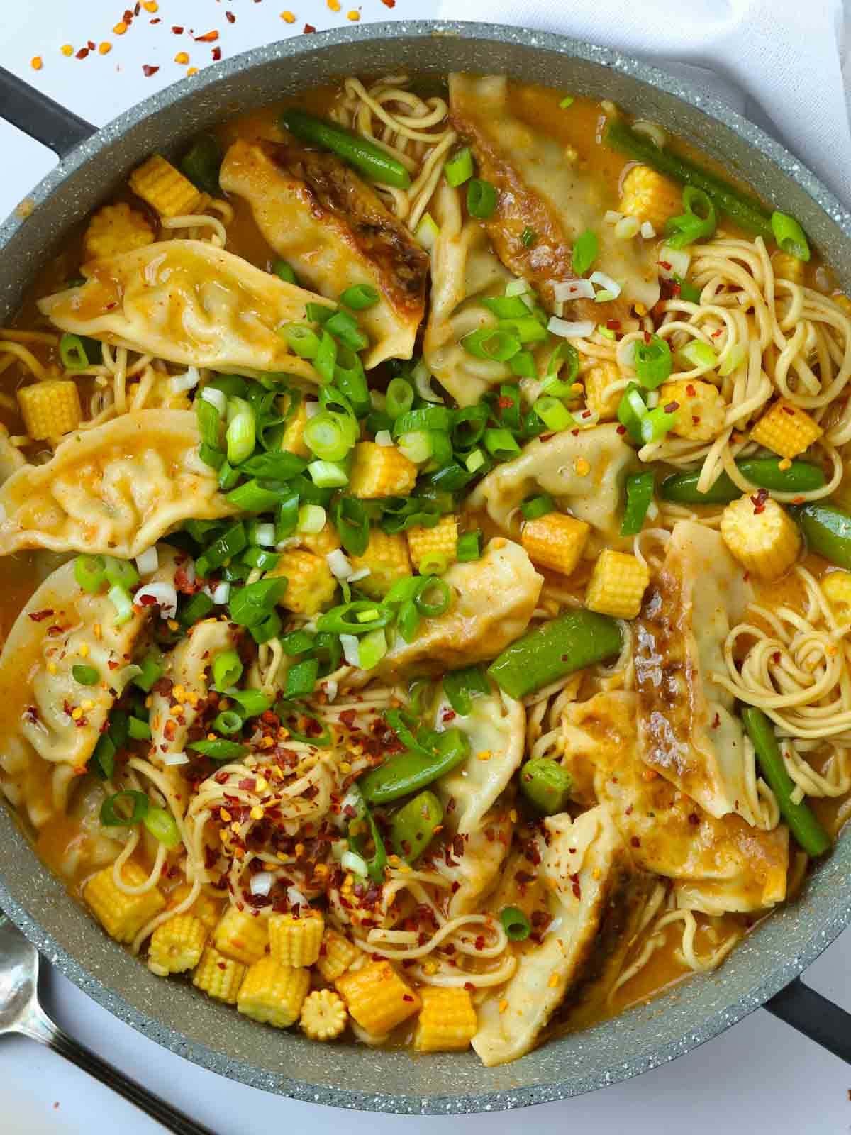 A pot filled with cooked Gyoza Soup, including dumplings, noodles, beans, corn and spring onions.