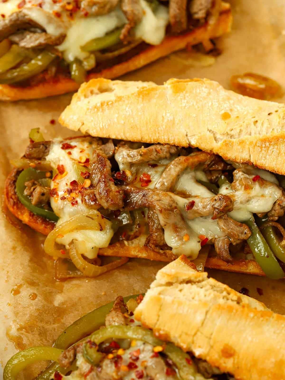 A closer look at the filling of a Philly Cheesesteak in a baguette. Steak, cheese, veggies and a sprinkle of chilli flakes.