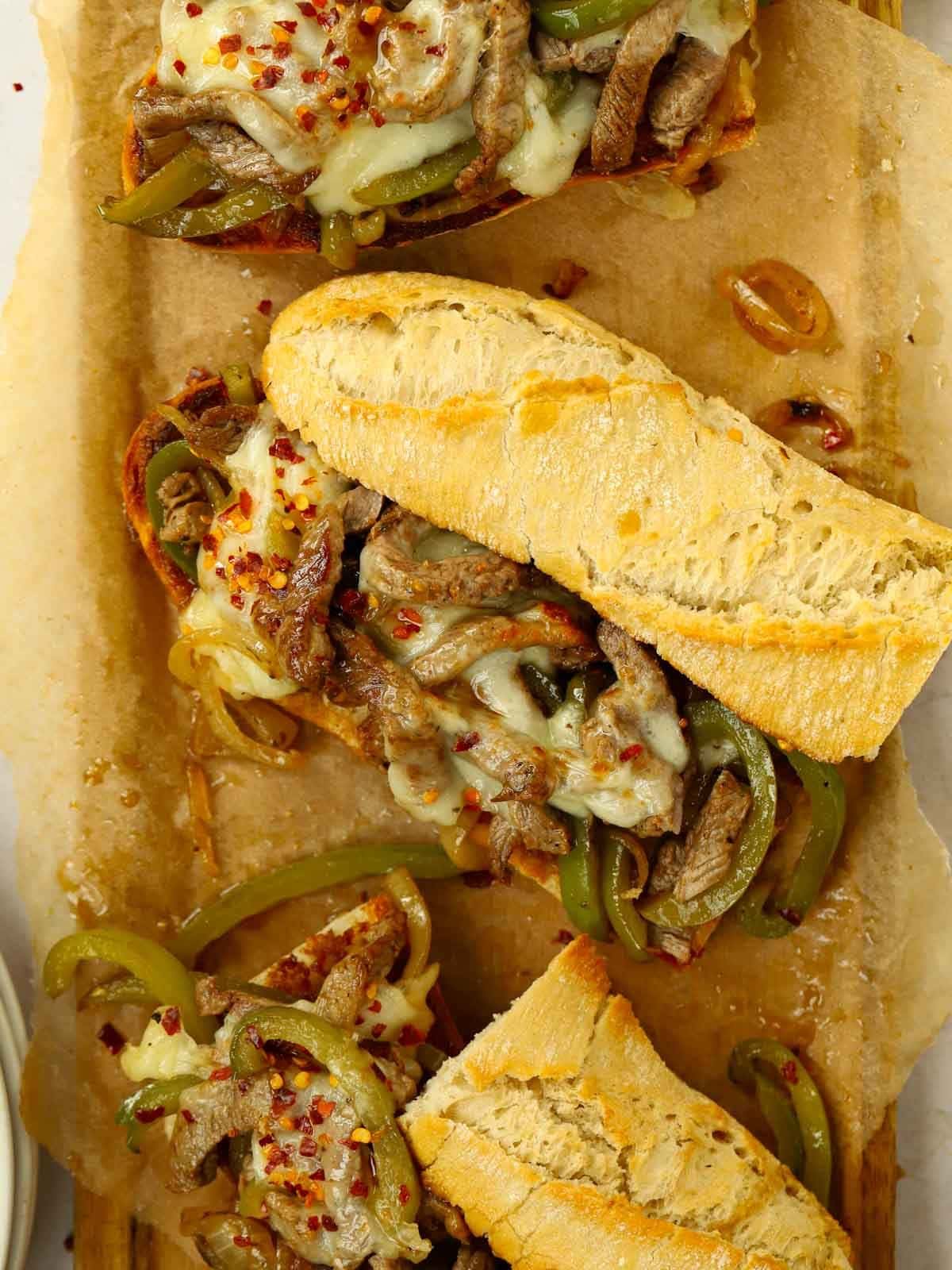 A board with three Philly Cheesesteak sandwiches ready to eat.