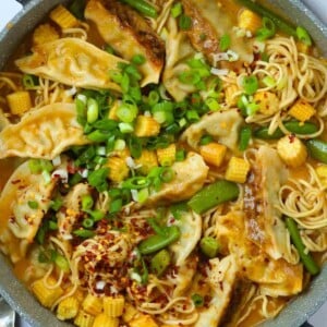 A pot filled with chunky Gyoza Soup, including noodles, dumplings and vegetables in a red Thai sauce.
