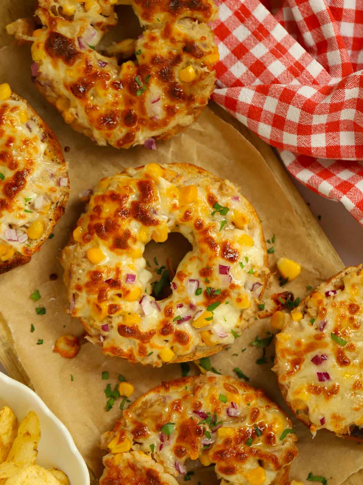 Halved bagels on a chopping board with tuna and melted cheese on top for the ultimate tuna melt lunch recipe.