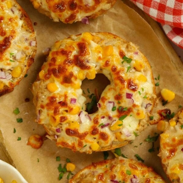 A bagel with a tuna melt topping on a board with sweetcorn.