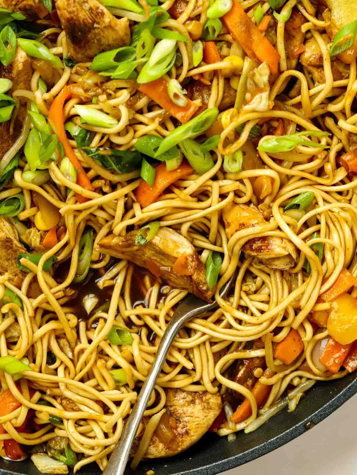 A close up of cooked noodles, chicken and vegetables in a dark, sticky Chinese-style sauce for a simple Chicken Chow Mein recipe.