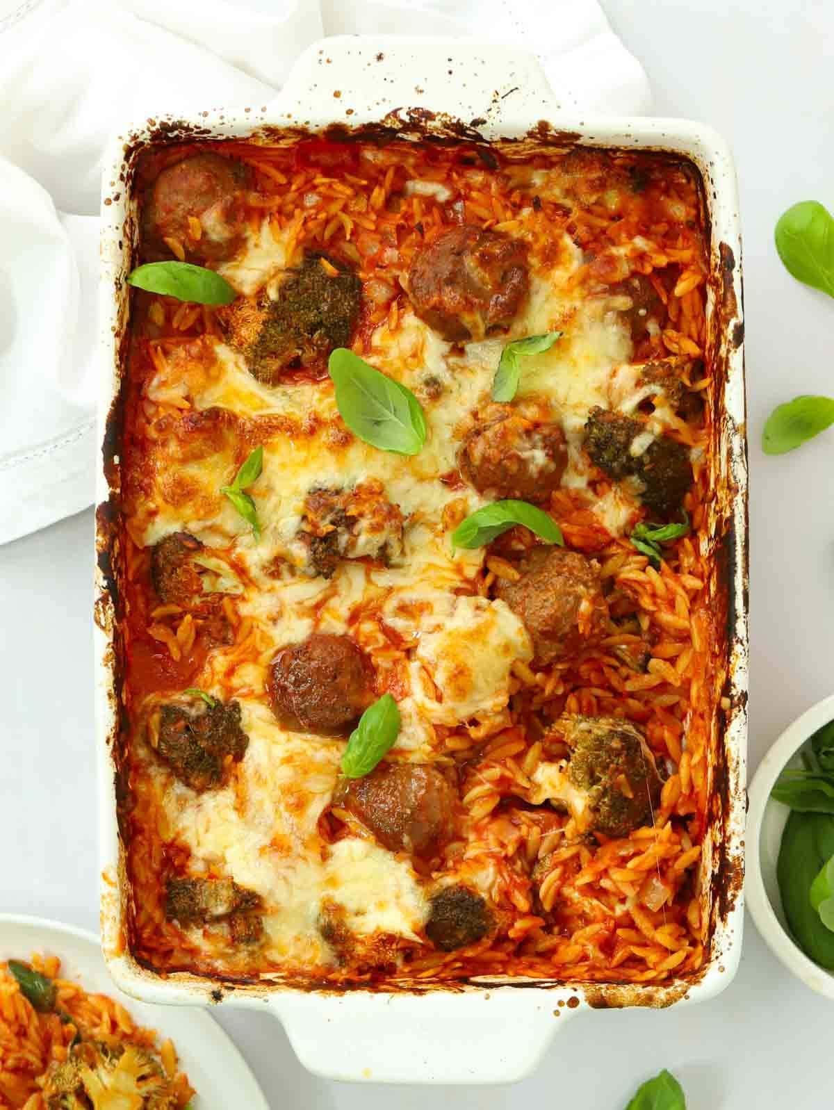 An oven dish filled with cooked Meatball Orzo Bake, straight out of the oven, topped with cheese and ready to serve.