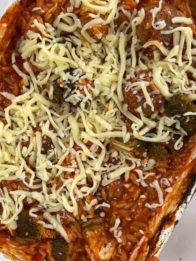 How to make Meatball Orzo Bake, step 4. Cheese is sprinkled over the dish with orzo, meatballs and broccoli in a tomato sauce.