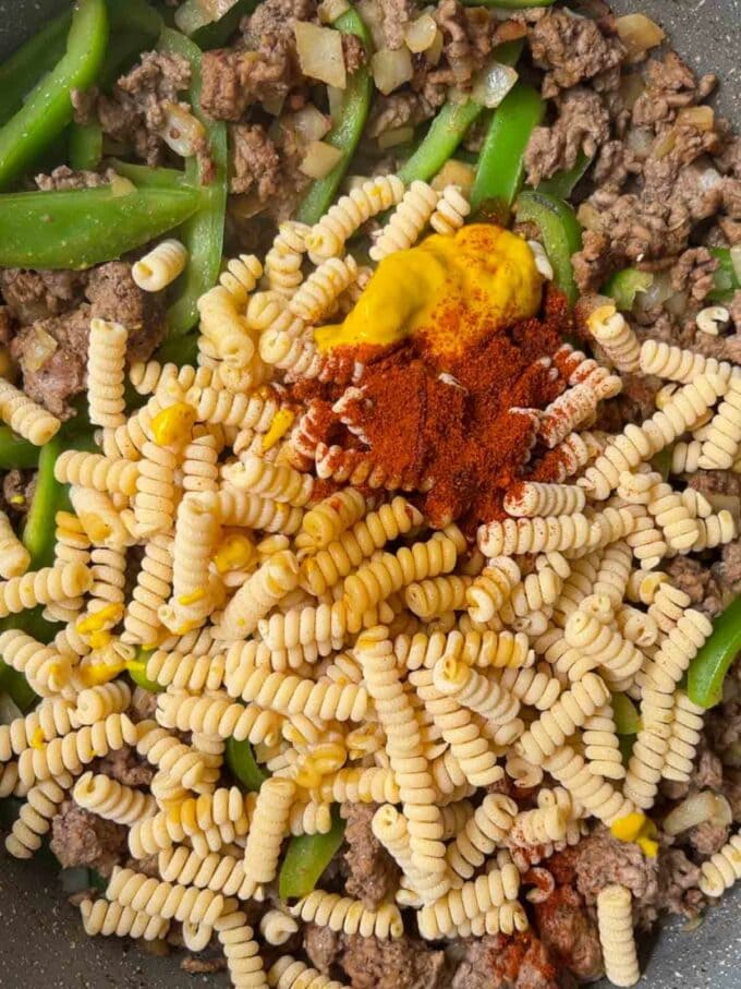 Mince, peppers and pasta cooking in a pan for step 2 of the recipe Cheeseburger Pasta.