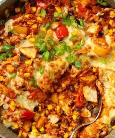 A round pan filled with chicken, rice, peppers, beans and topped with melted cheese for a Mexican chicken recipe.