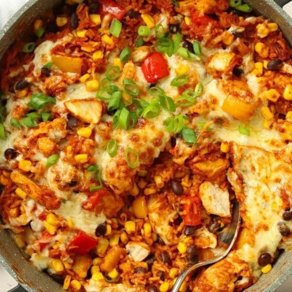 A round pan filled with chicken, rice, peppers, beans and topped with melted cheese for a Mexican chicken recipe.