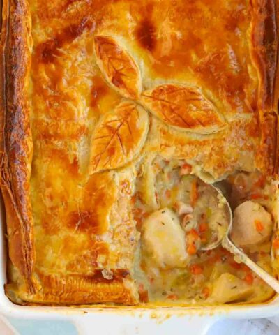 A close up of a creamy chicken and bacon pie, with a spoon in ready to serve a portion. A creamy filling shown inside.