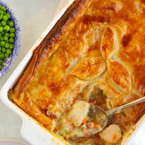 A table with a chicken pie on top being served with a spoon, with a bowl of peas on the side.