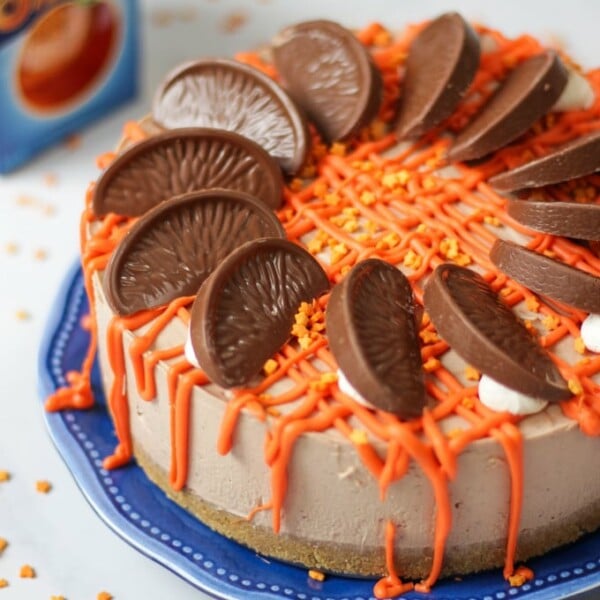A side angle of a chocolate orange cheesecake on a plate, ready to be sliced and served. Orange piping and chocolate segments decorate the top.