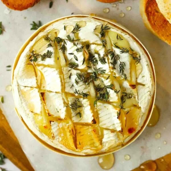 A close up of a camembert wheel with honey and thyme and garlic on top.