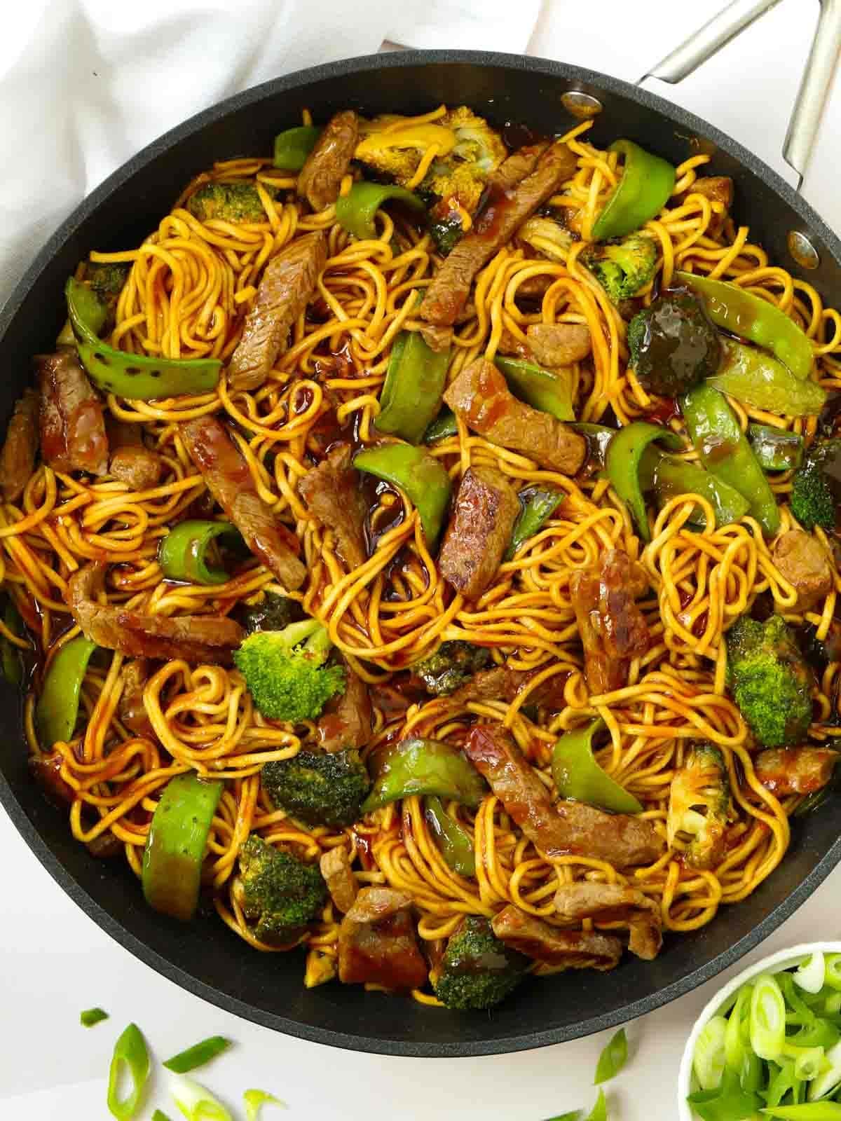 A big pan filled with sticky beef and noodles, as well as green vegetables and a dark sauce.