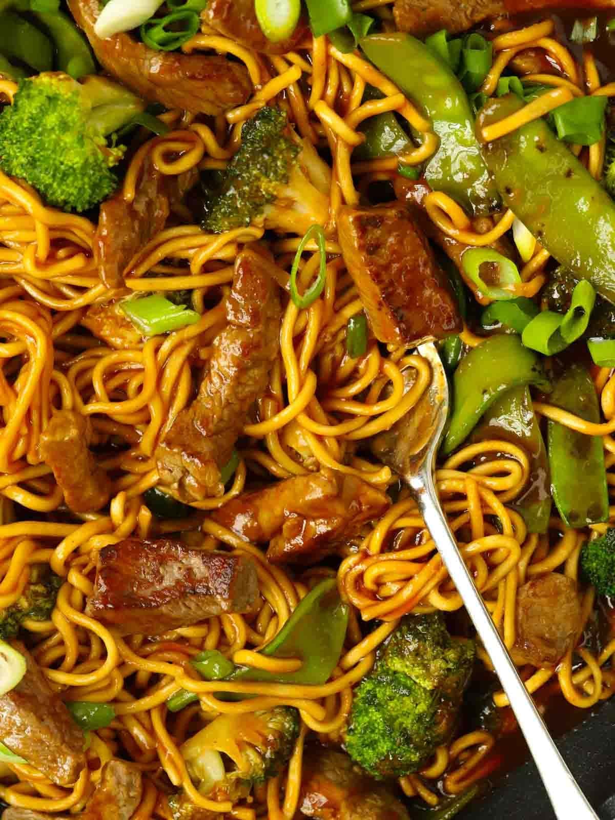 A fork stuck into noodles, with steak and vegetables amongst it.
