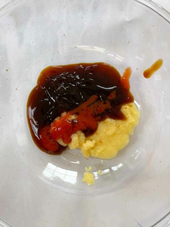 Sauce ingredients in a glass bowl, made up of ginger, oyster sauce, soy sauce, honey and tomato sauce.