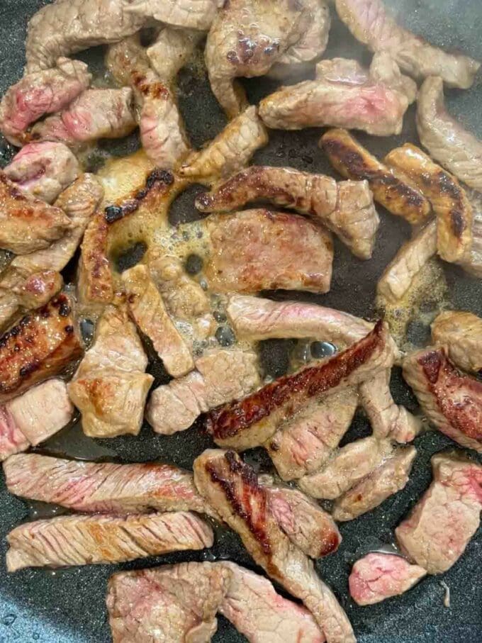 Steak frying in a pan with oil.