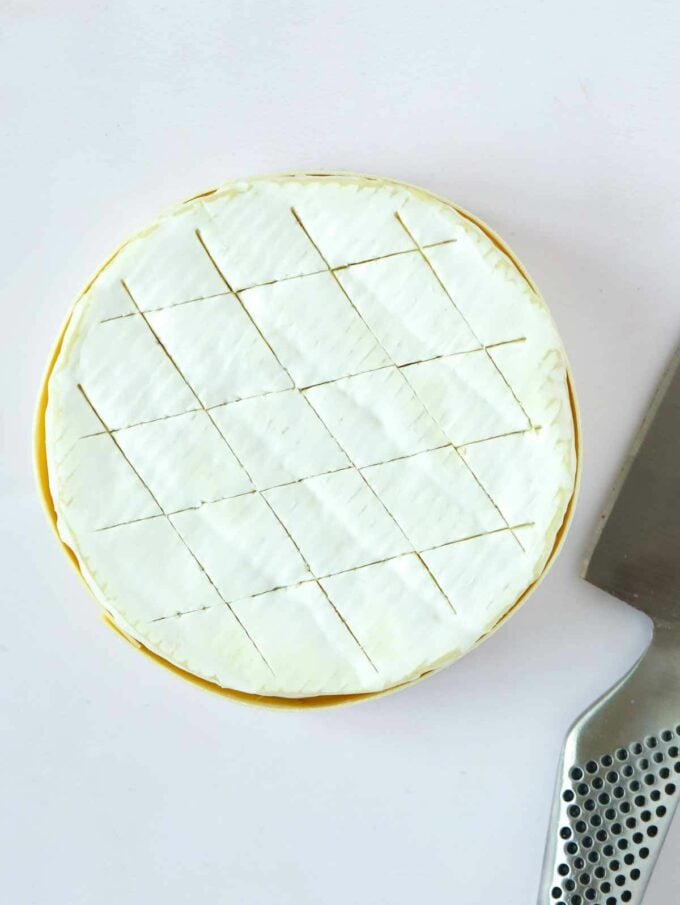 A round of camembert cheese with criss-cross pattern scored into the rind.