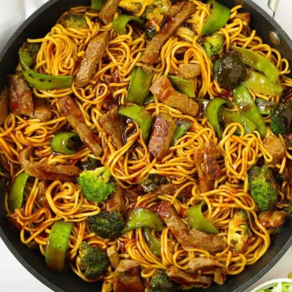 A round pan filled with noodles, steak, green vegetables and sauce for the recipe Sticky Beef and Noodles.
