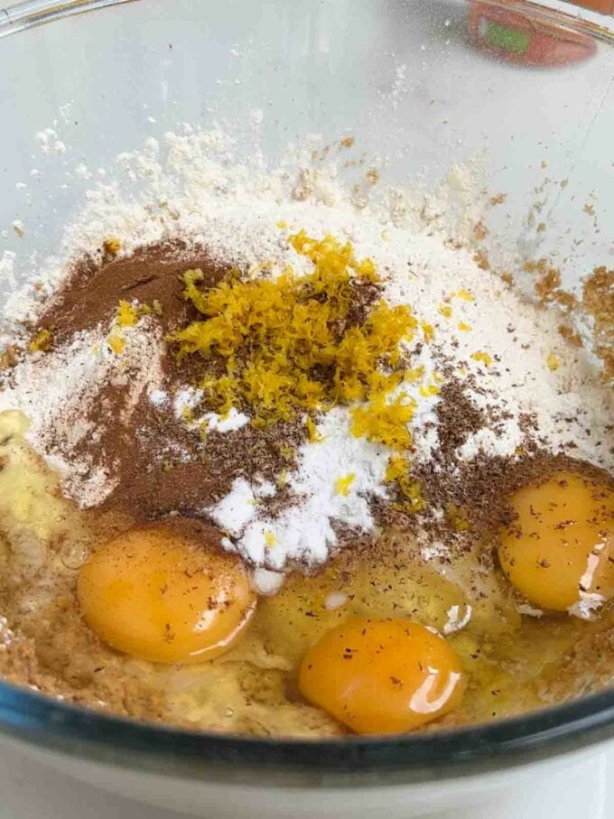 A glass bowl filled with ingredients for Pumpkin Cake. Three raw eggs on top of brown sugar, butter, flour, lemon zest, nutmeg and cinnamon.