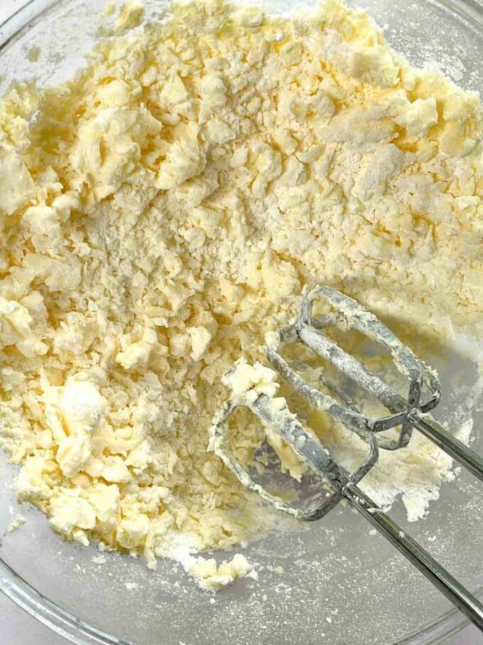 Butter and icing sugar whisked together in a glass bowl for the recipe Cream Cheese Frosting.