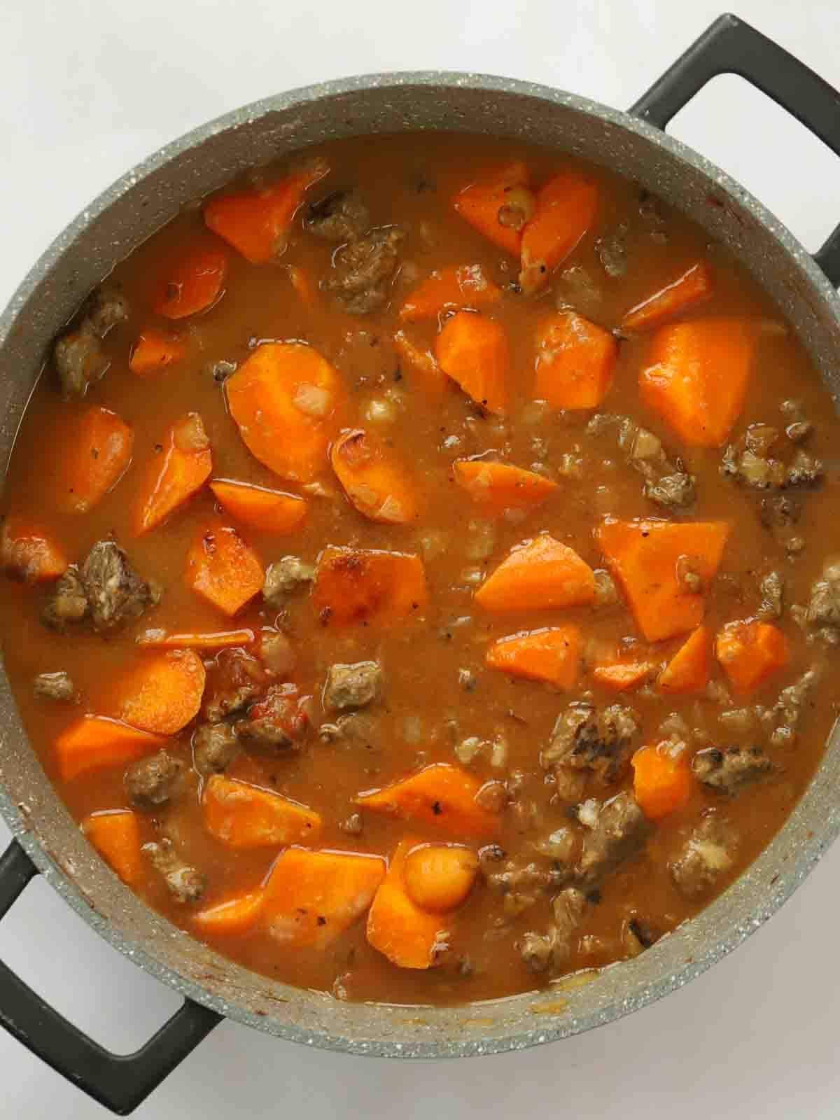 Cooked beef and carrots in a rich gravy in a large pan for step 3 in the recipe for Steak Pie.